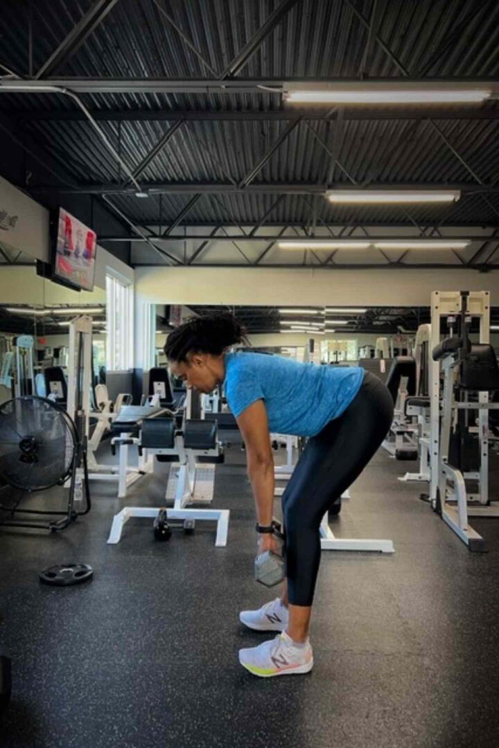 woman standing in black leggings and blue shirt doing deadlifts
