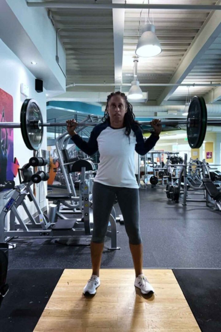 woman standing in squat rack with barbell on upper back for barbell squats