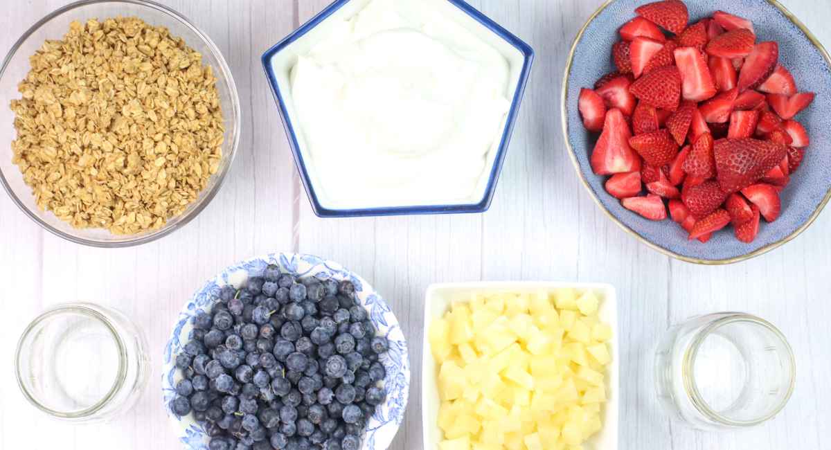 yogurt parfait ingredients on a counter including fresh fruit, granola and yogurt