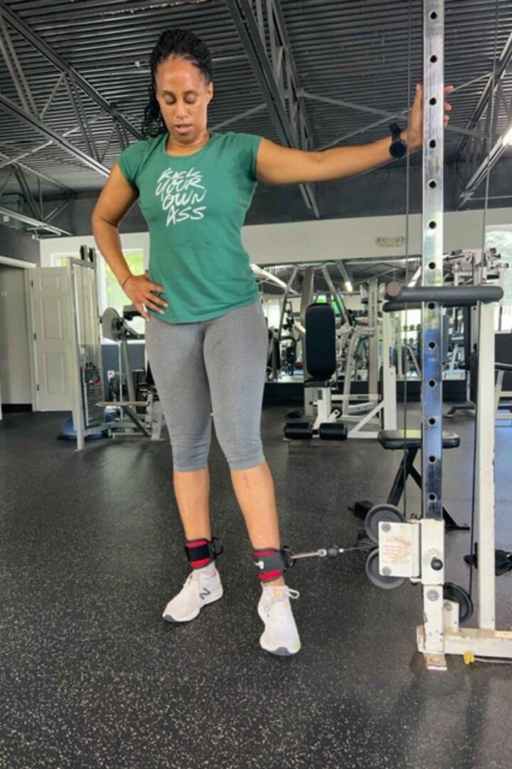 woman in green tshirt and gray leggings cable adduction leg exercise
