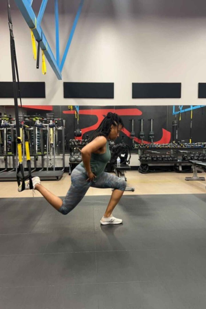 woman in leggings doing TRX bulgarian split squats in the gym