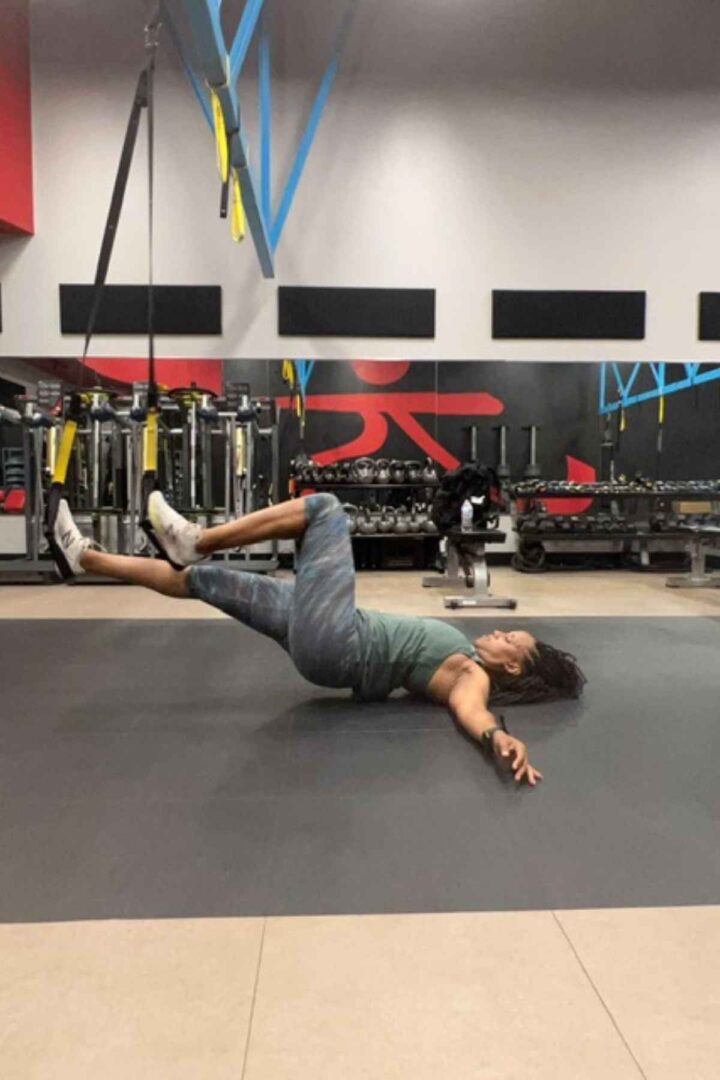 woman on the floor of the gym doing TRX hamstring curls