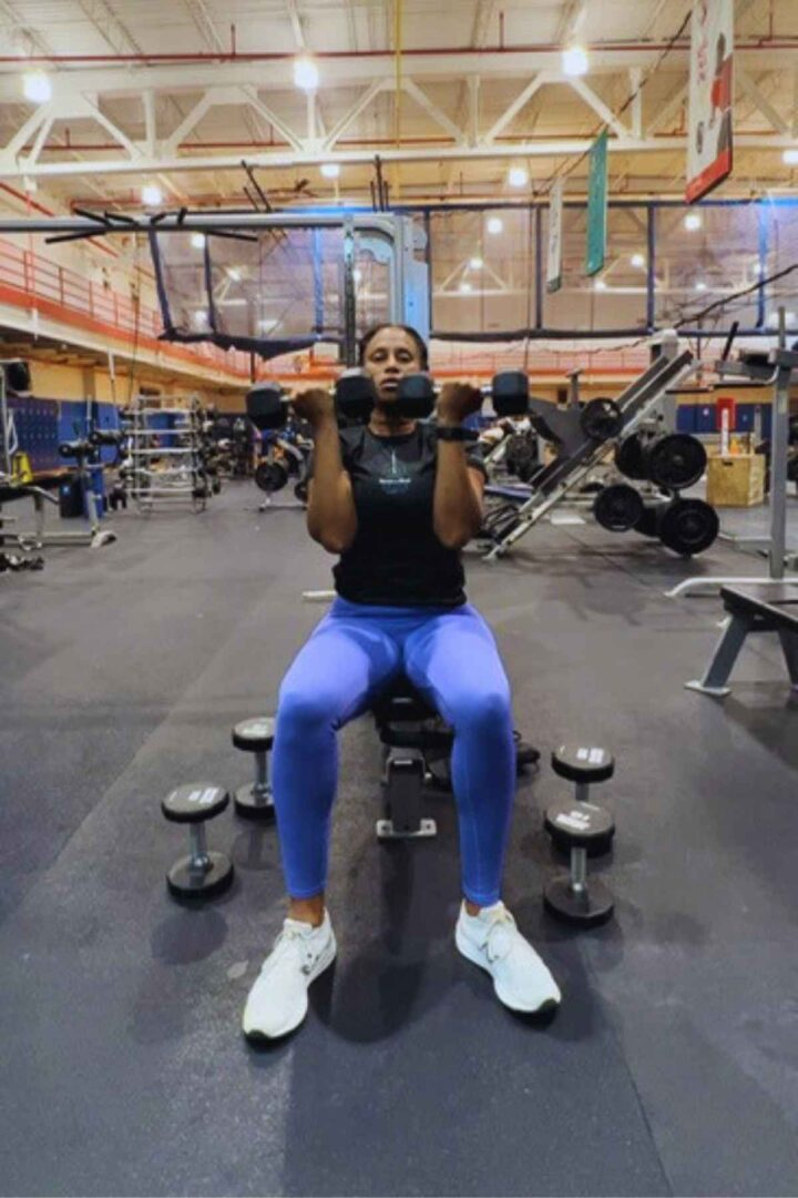 woman sitting on bench in gym doing arnold press exercise in shoulder workout