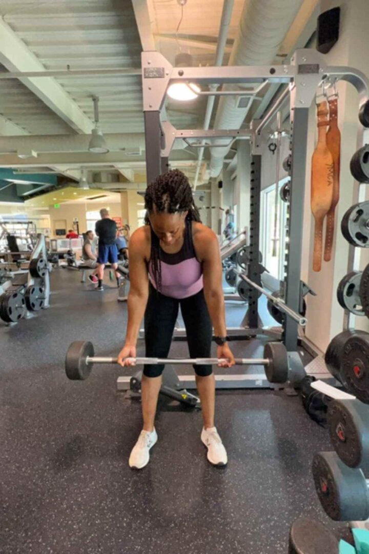 woman in purple tank doing barbell rows in back and bicep pull workout