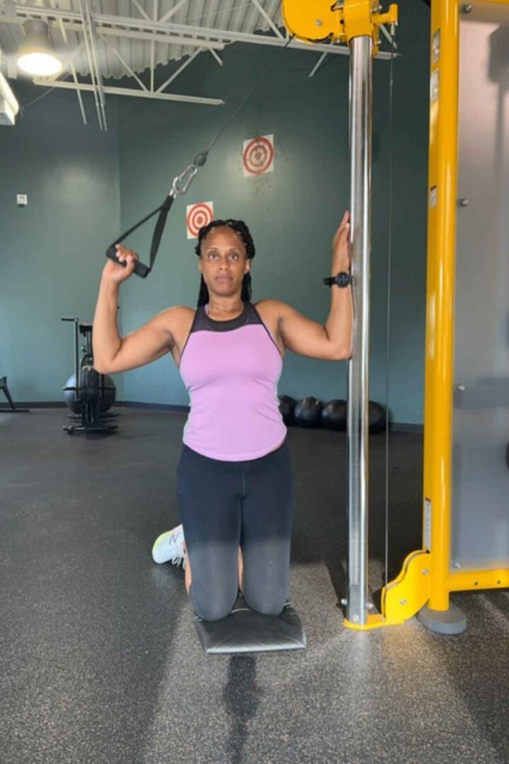 woman in purple tank doing single arm lat pull down
