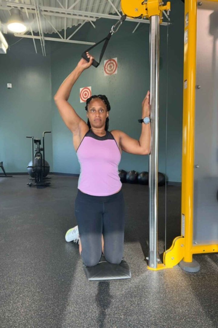 woman in purple tank doing single arm lateral pull down