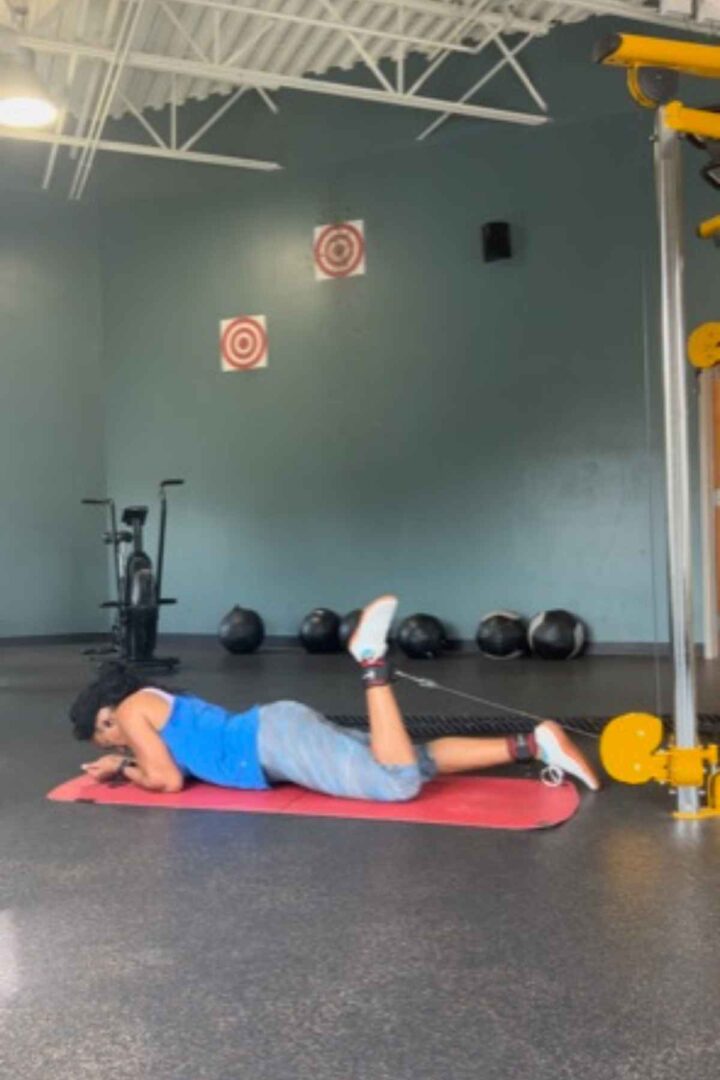 woman on the floor doing hamstring curls cable machine leg exercises